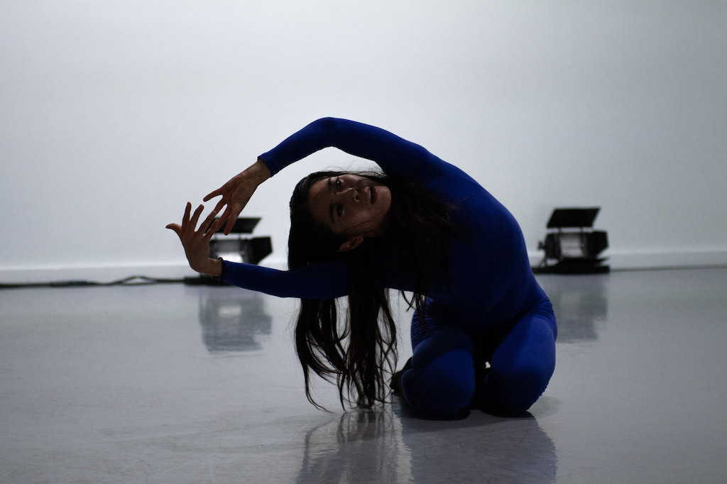 Dancer training in a dance studio, seated on the floor with one arm extended over her head